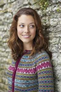 Blacker Yarns The Knitter Features Jura Cardigan in Tamar Lustre Yarn Woman standing against wall wearing fair isle cardigan